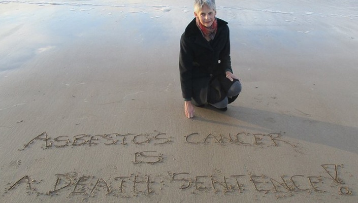 person writing message on the sand that says "asbestos cancer is a death sentence"