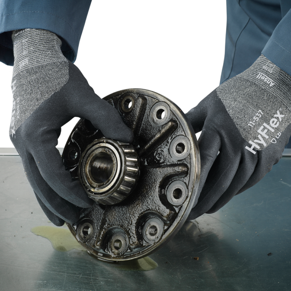 Close-up of Ansell HyFlex 11-537 gloves handling an oily metal component in a workshop setting