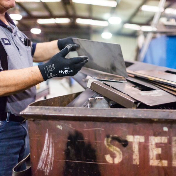 Worker wearing Ansell HyFlex 11-542 gloves while handling sharp metal sheet in workshop