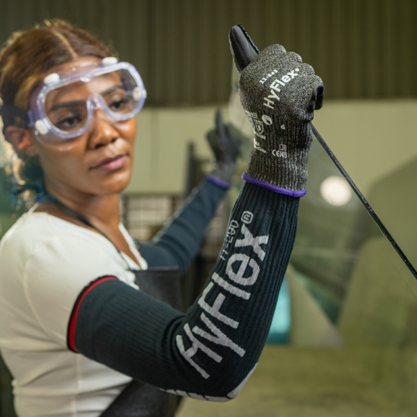 Worker wearing Ansell HyFlex 11-543 gloves and protective sleeves while handling glass in an industrial setting.