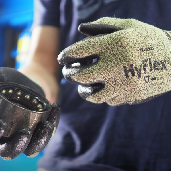 Ansell HyFlex 11-550 gloves in use, gripping an industrial bearing in a maintenance setting.