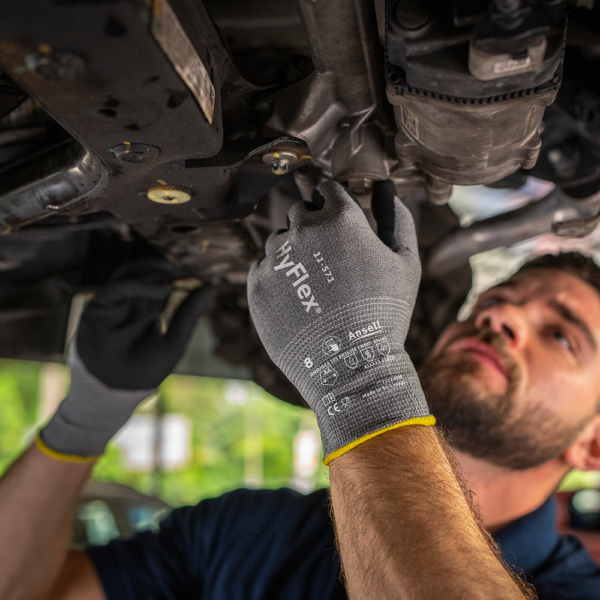 Worker wearing Ansell HyFlex 11-571 gloves while performing mechanical work under a vehicle