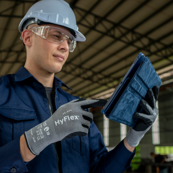 Industrial worker wearing HyFlex 11-571 gloves while operating a touchscreen tablet on site