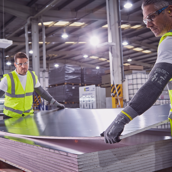 Two workers handling sheet metal while wearing Ansell HyFlex 11-581 gloves and protective gear in a warehouse