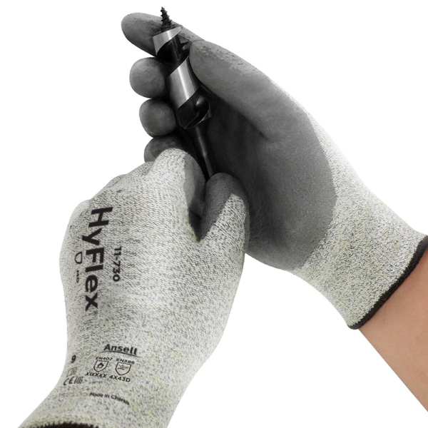 Hands wearing Ansell HyFlex 11-730 gloves handling a sharp drill bit for precision work