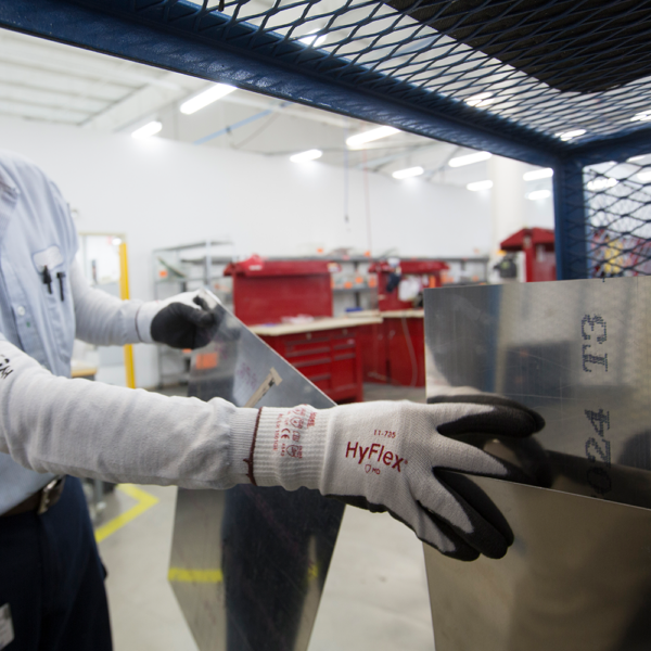 Worker wearing Ansell HyFlex 11-735 gloves handling sheet metal in an industrial workshop