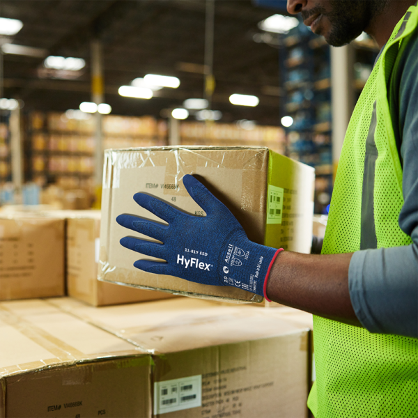 Worker wearing Ansell HyFlex 11-819 ESD gloves while handling cardboard boxes in a warehouse
