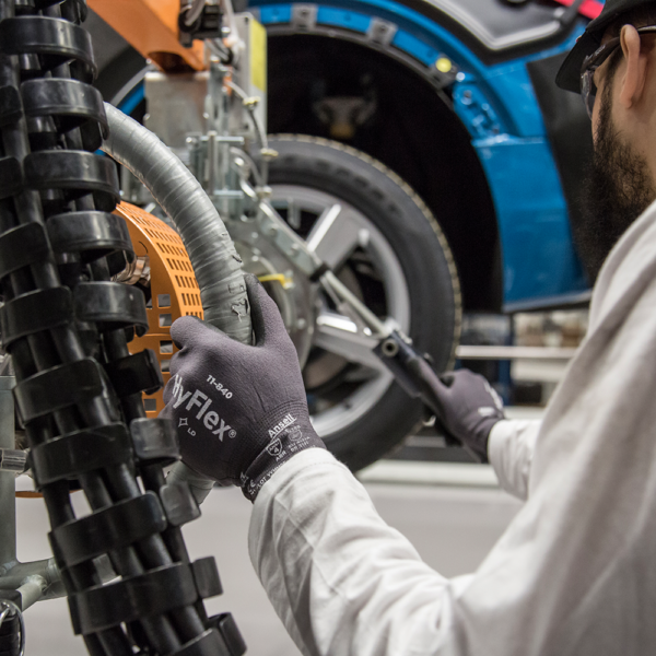 Technician using HyFlex 11-840 gloves during automotive assembly near a vehicle chassis.