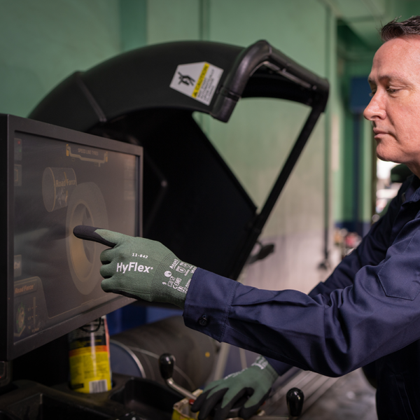 Worker wearing HyFlex 11-842 gloves operating touchscreen machinery in a workshop