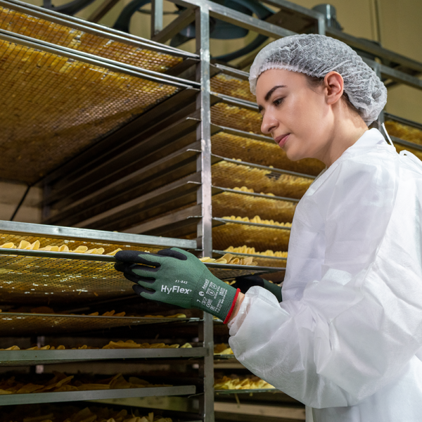 Worker wearing HyFlex 11-842 gloves inspecting food trays in a processing facility