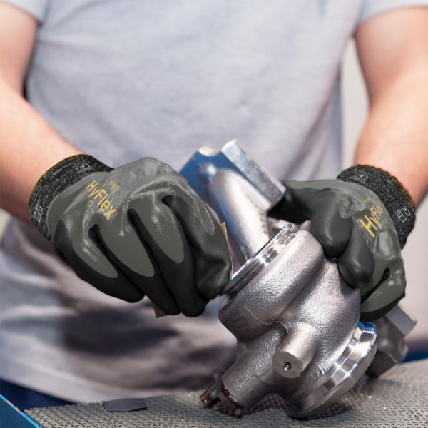 Ansell HyFlex 11-939 gloves in use, handling a precision metal component in a workshop environment.