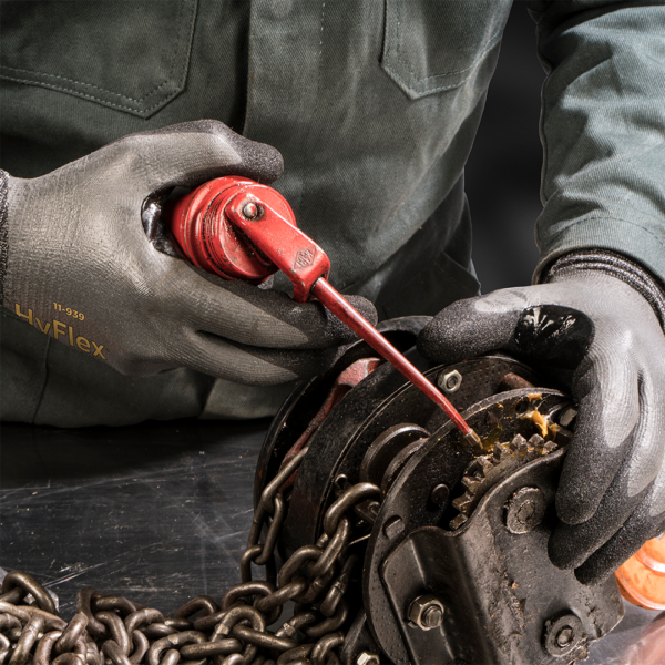 Worker using Ansell HyFlex 11-939 gloves while applying lubricant to a mechanical chain assembly.