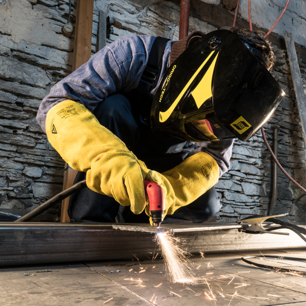 Worker wearing Ansell ActivArmr 43-216 gloves while operating a welding torch in an industrial setting