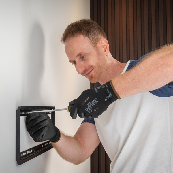 Person wearing HyFlex 48-101 gloves while mounting a TV bracket, demonstrating use in home DIY tasks.