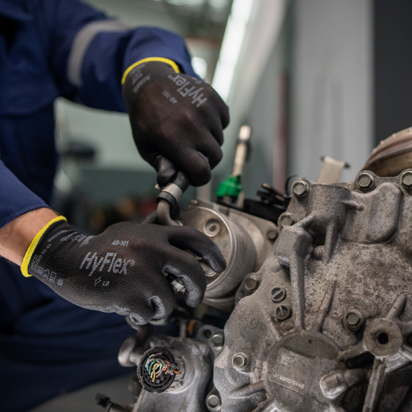 Mechanic using HyFlex 48-101 gloves to perform detailed automotive repair, showcasing grip and tactile control in oily environments.