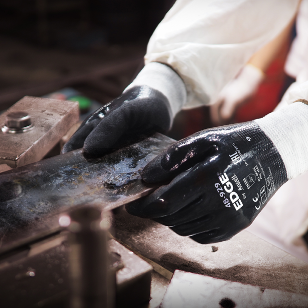 Ansell EDGE 48-929 gloves in use handling oily metal sheet in an industrial environment.