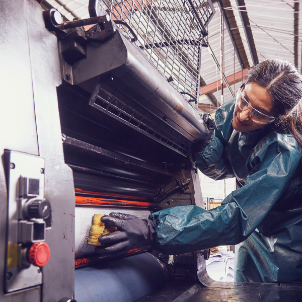 Worker wearing Ansell AlphaTec 53-002 gloves while cleaning industrial printing press.