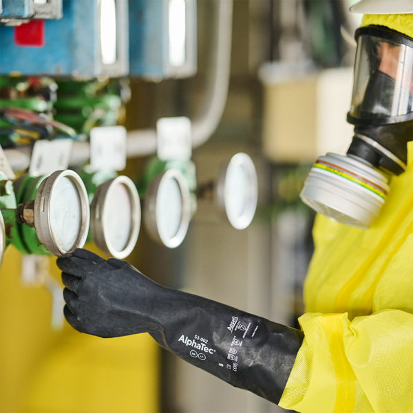Operator in hazchem suit and Ansell AlphaTec 53-002 gloves working with control gauges.