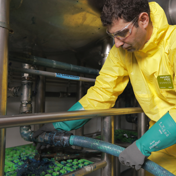 Worker wearing yellow coveralls and Ansell AlphaTec 58-435 gloves while handling chemical equipment in an industrial setting.