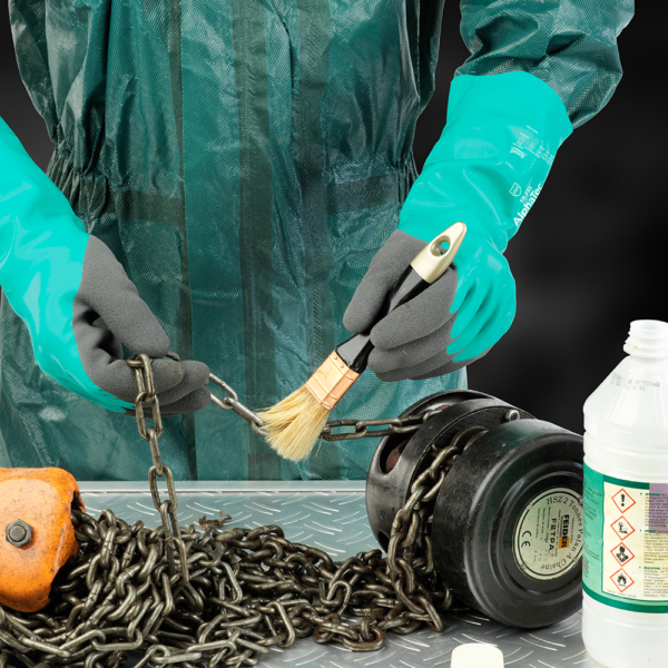 Person wearing Ansell AlphaTec 58-735 gloves brushing a metal chain, showcasing dexterity and chemical resistance.