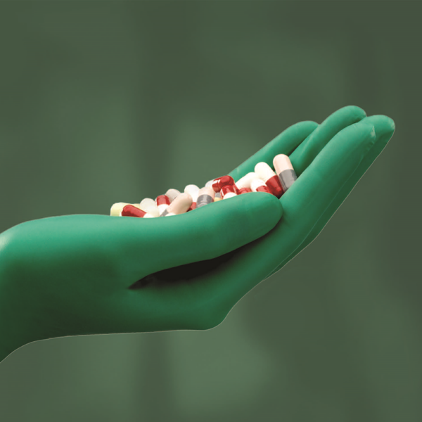 Green nitrile-gloved hand holding pharmaceutical capsules