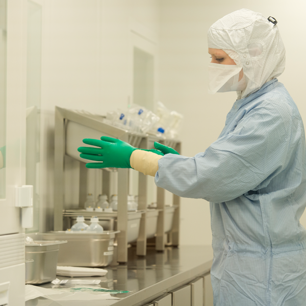 Person in cleanroom applying double gloves, including green nitrile gloves over inner gloves