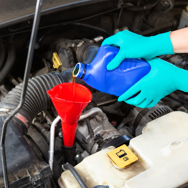 Person wearing protective nitrile gloves pouring engine oil into a car using a red funnel