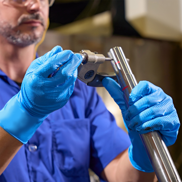 Worker using blue nitrile Microflex 93-283 gloves to handle metal parts in an industrial setting.