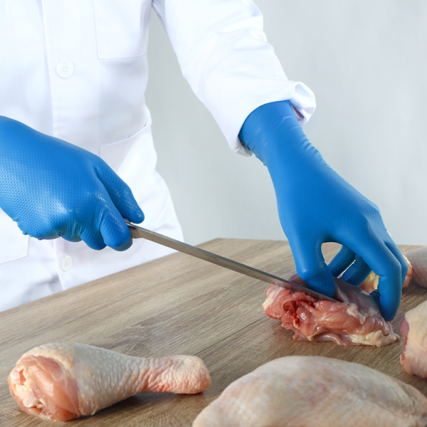 Food handler using Microflex 93-283 nitrile gloves to cut raw chicken on a wooden surface.