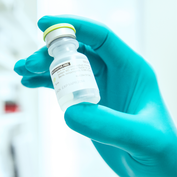 Close-up of teal nitrile glove securely holding pharmaceutical vial in clean lab environment.