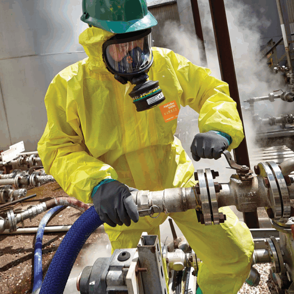 Industrial worker wearing AlphaTec gloves and chemical protective suit while tightening valve in hazardous environment
