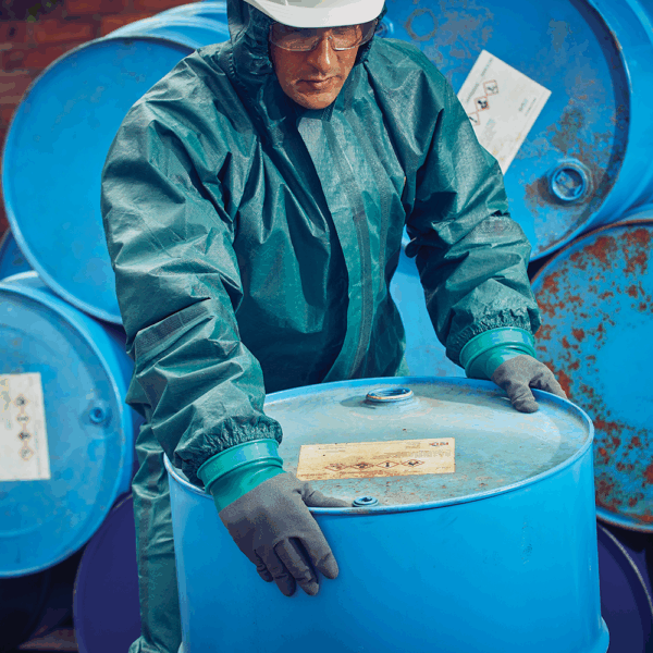 Worker using Ansell AlphaTec gloves to safely handle hazardous material drums in chemical storage facility