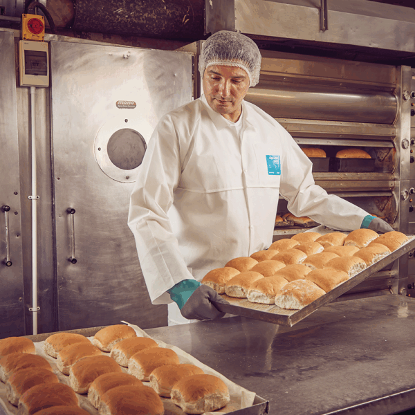 Food industry worker wearing AlphaTec protective gloves while handling trays of fresh bread rolls