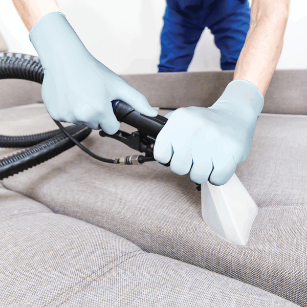 Worker wearing Ansell MICROFLEX 82-134 nitrile gloves cleaning a sofa using a vacuum extraction tool.