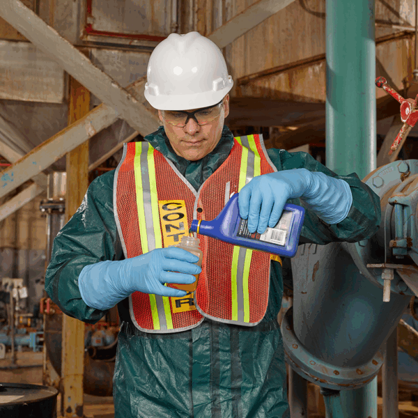 Worker wearing Ansell MICROFLEX 93-243 nitrile gloves and safety gear pouring liquid chemicals in an industrial environment.
