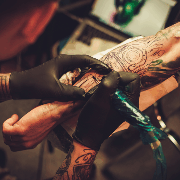 Tattoo artist wearing Ansell MICROFLEX 93-732 black nitrile gloves while tattooing a client’s arm in a professional studio.