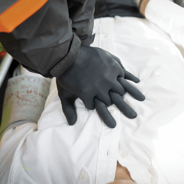 First responder wearing Ansell MICROFLEX 93-732 black nitrile gloves performing CPR chest compressions.