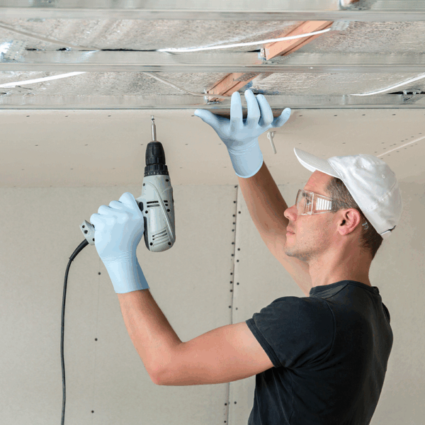 Tradesperson wearing Ansell MICROFLEX 93-833 nitrile gloves using a power drill for ceiling installation work.