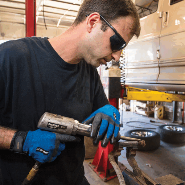 Worker wearing Ansell ActivArmr AN97003 gloves operating an air-powered impact tool during mechanical repair work.