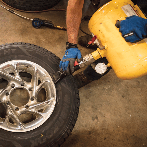 Mechanic wearing Ansell ActivArmr AN97003 gloves inflating a vehicle tyre using a compressed air tank in an auto workshop.