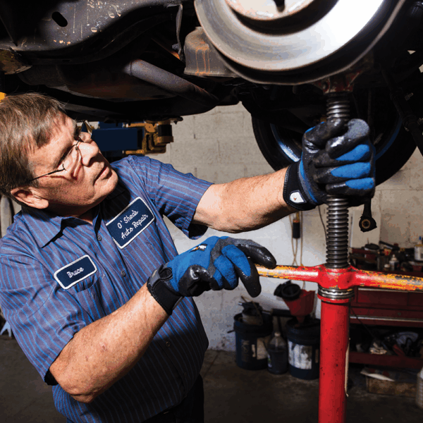 Automotive technician wearing Ansell ActivArmr AN97003 gloves while adjusting a car jack stand in a workshop environment.