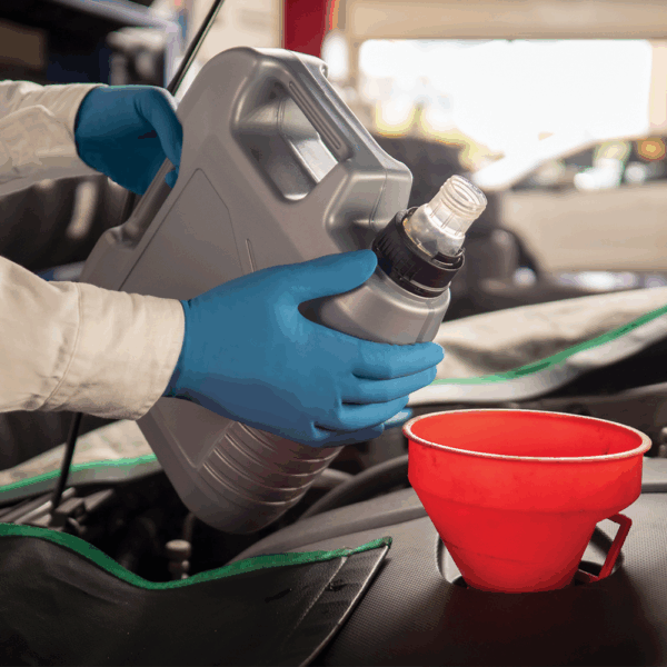 Worker wearing Ansell MICROFLEX 93-375 gloves pouring engine oil from a container into a vehicle using a red funnel.